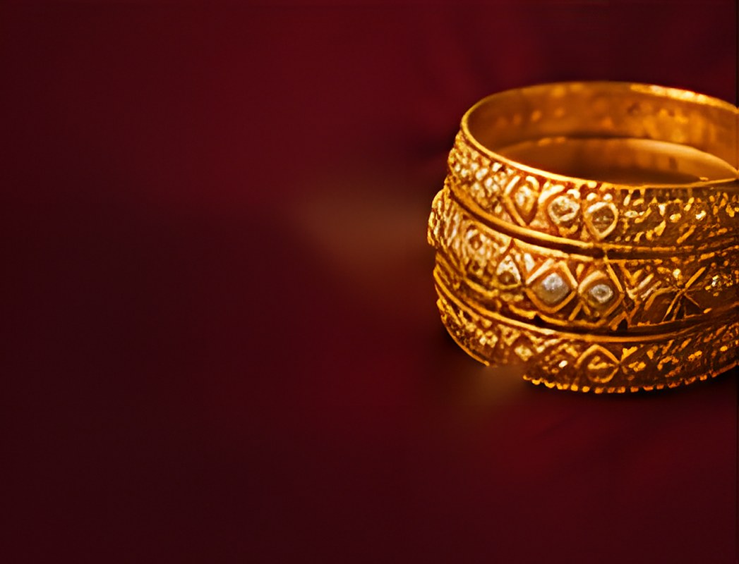 Stack of engraved gold bangles on maroon silk